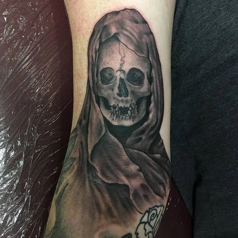 Black and grey tattoo of a hooded reaper with a skull face beneath the cowl, dripping shadow, on the forearm, by Christian "Tiki" Ramos at Ohana Tattoo Company, Waikiki, Hawaii.