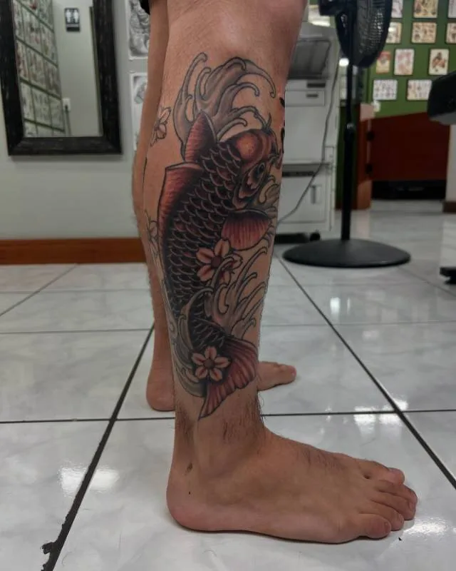 Black and grey Japanese koi tattoo climbing the calf through waves and cherry blossoms, by Christian "Tiki" Ramos at Ohana Tattoo Company, Waikiki, Hawaii.