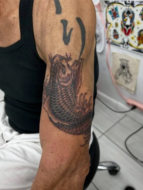Black and grey Japanese koi tattoo descending the bicep with detailed scale work and a fan of fins, by Christian "Tiki" Ramos at Ohana Tattoo Company, Waikiki, Hawaii.