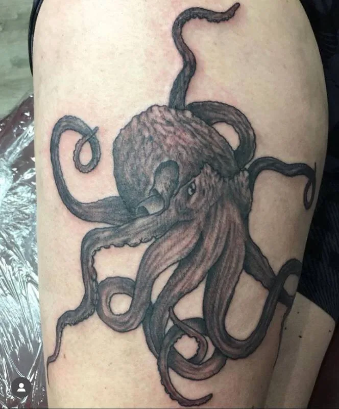 Black and grey tattoo of an octopus with eight sprawling, curling tentacles on an upper arm, by Christian "Tiki" Ramos at Ohana Tattoo Company, Waikiki, Hawaii.
